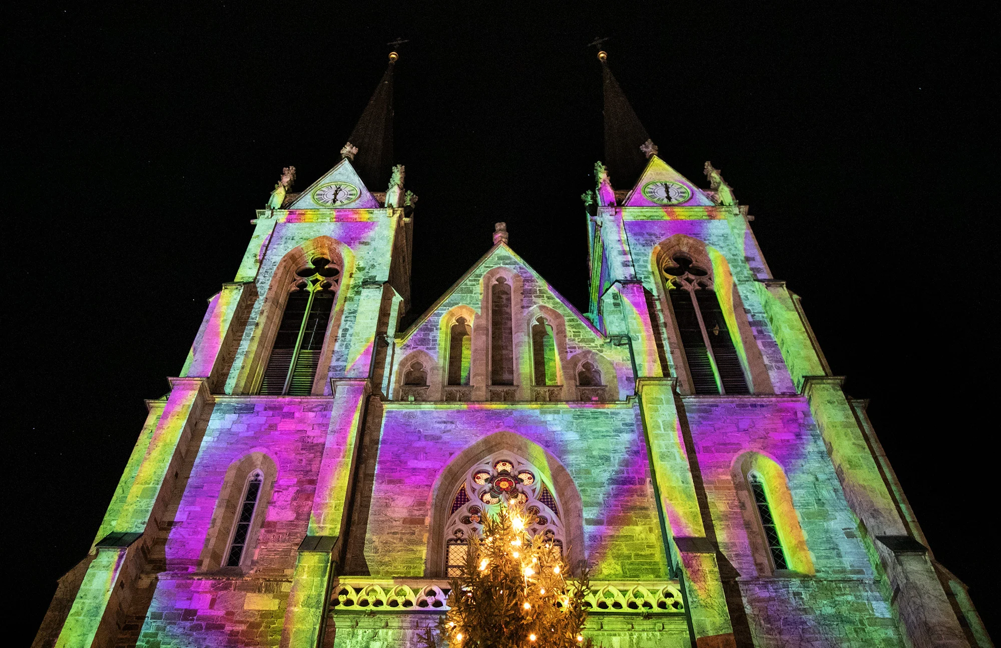 Bunte Fassadenprojektion am Dom mit beleuchtetem Baum vor dem Eingang