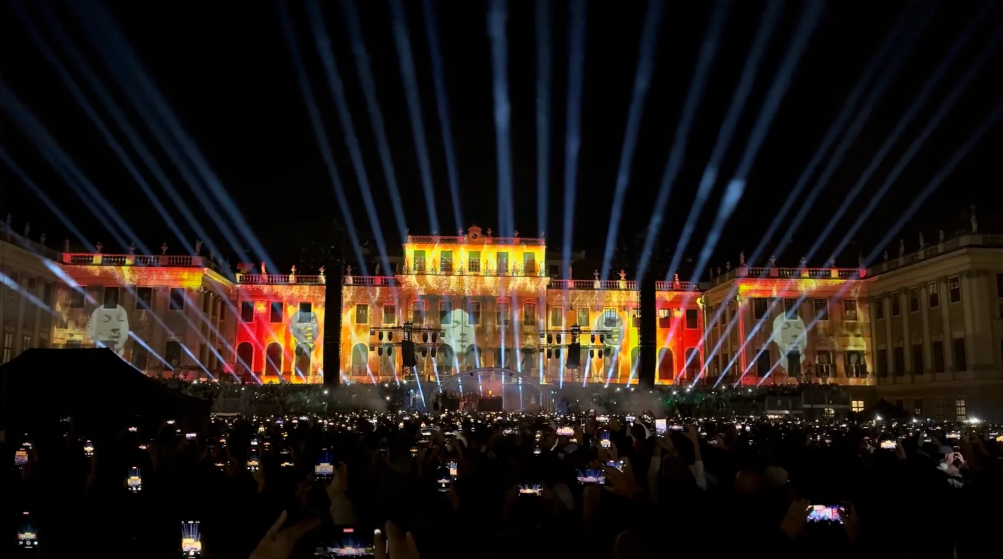 Konzertpublikum vor goldfarbenen Visuals und Lichtstrahlen am Schloss Schönbrunn