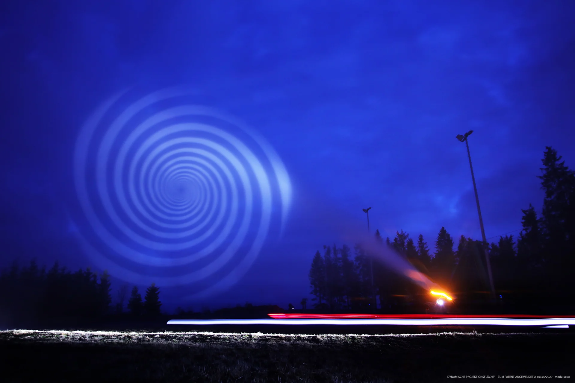 Weiße Spiralprojektion auf blau beleuchtete Wasserpartikel im Freien