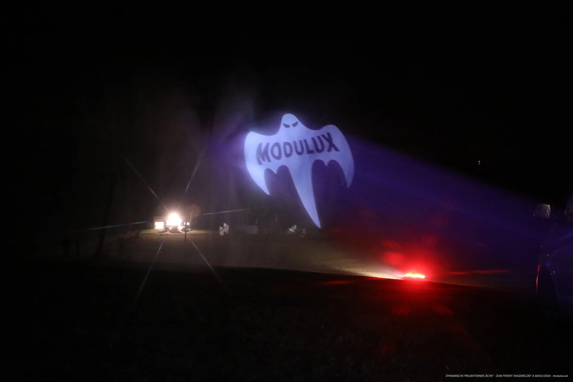 Weite Nachtaufnahme der MODULUX-Ghost-Projektion mit roten und weißen Lichtquellen