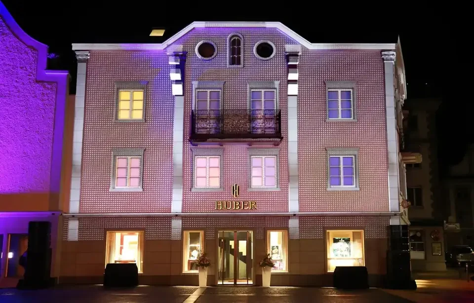 Beleuchtete Gebäudefassade mit sichtbaren Fenstern und Balkonen – HUBER OPENING, Huber Fine Watches & Jewellery, Bregenz, Österreich