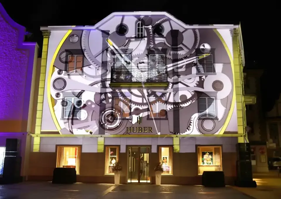 Uhrwerk und Zahnräder als Projektion auf die Fassade – HUBER OPENING, Huber Fine Watches & Jewellery, Bregenz, Österreich