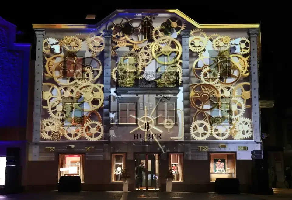 Uhrwerk und Zahnräder als Projektion auf die Fassade – HUBER OPENING, Huber Fine Watches & Jewellery, Bregenz, Österreich