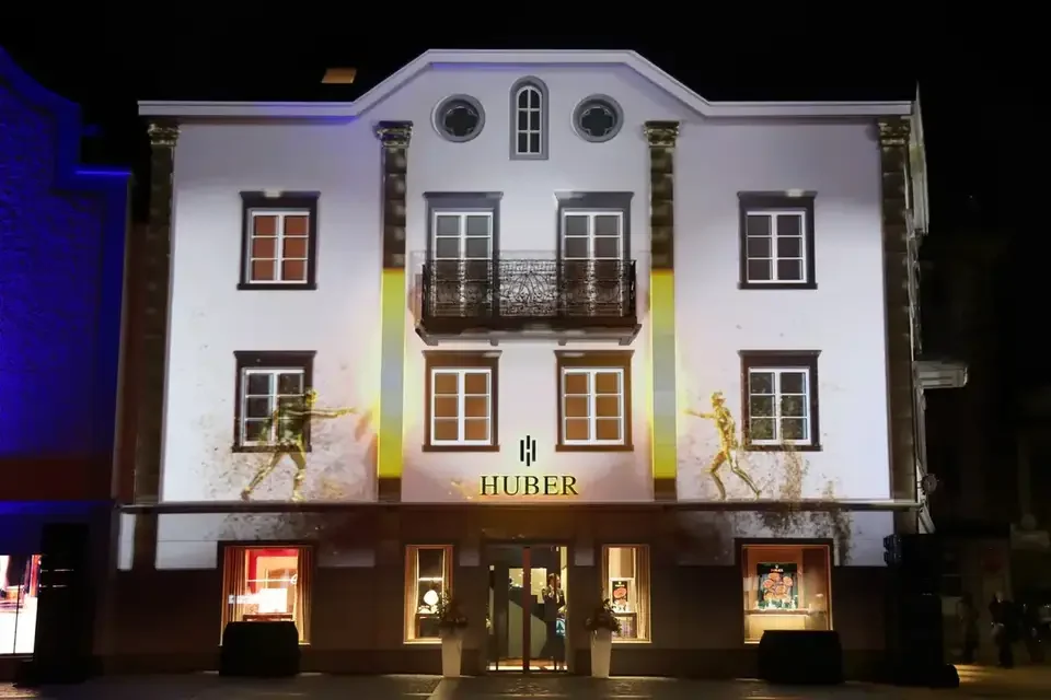 Weiße Fassadenprojektion mit architektonischen Konturen – HUBER OPENING, Huber Fine Watches & Jewellery, Bregenz, Österreich
