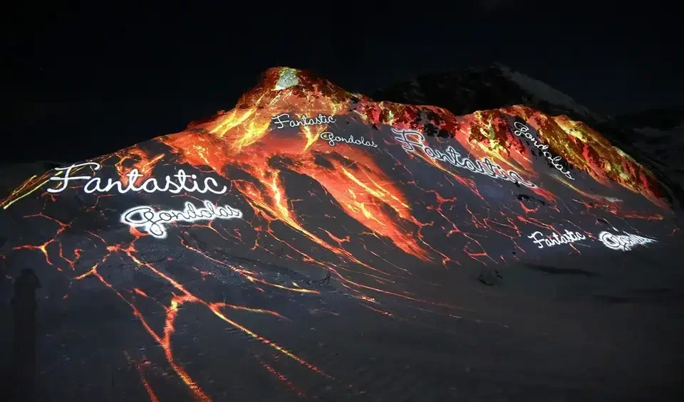 Feuer- und Lavamotive als Großbildprojektion auf einen verschneiten Berg – FANTASTIC GONDOLAS, Lech, Österreich
