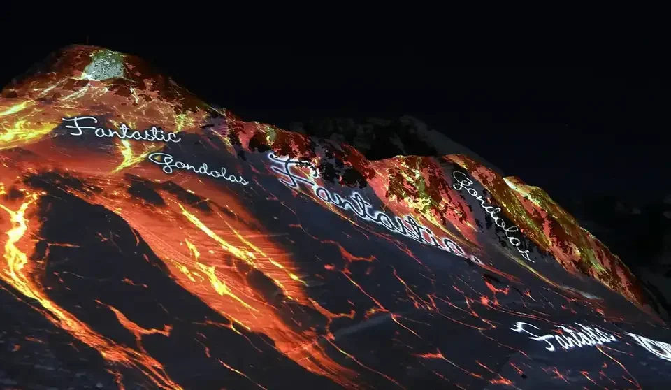 Feuer- und Lavamotive als Großbildprojektion auf einen verschneiten Berg – FANTASTIC GONDOLAS, Lech, Österreich