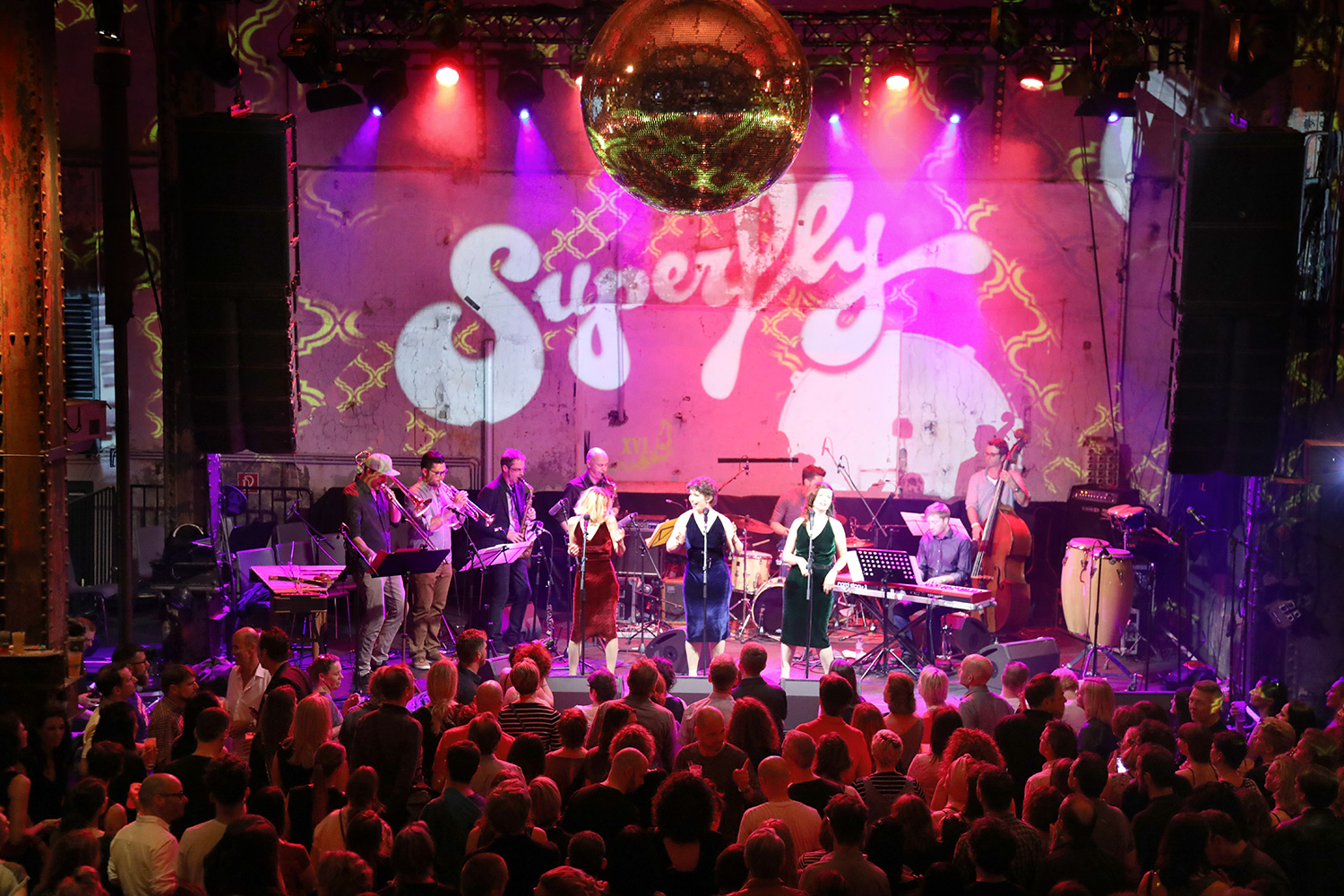 Band vor einer pinken Superfly-Projektion auf der Bühne – Superfly, Ottakringer Brauerei, Wien, Österreich