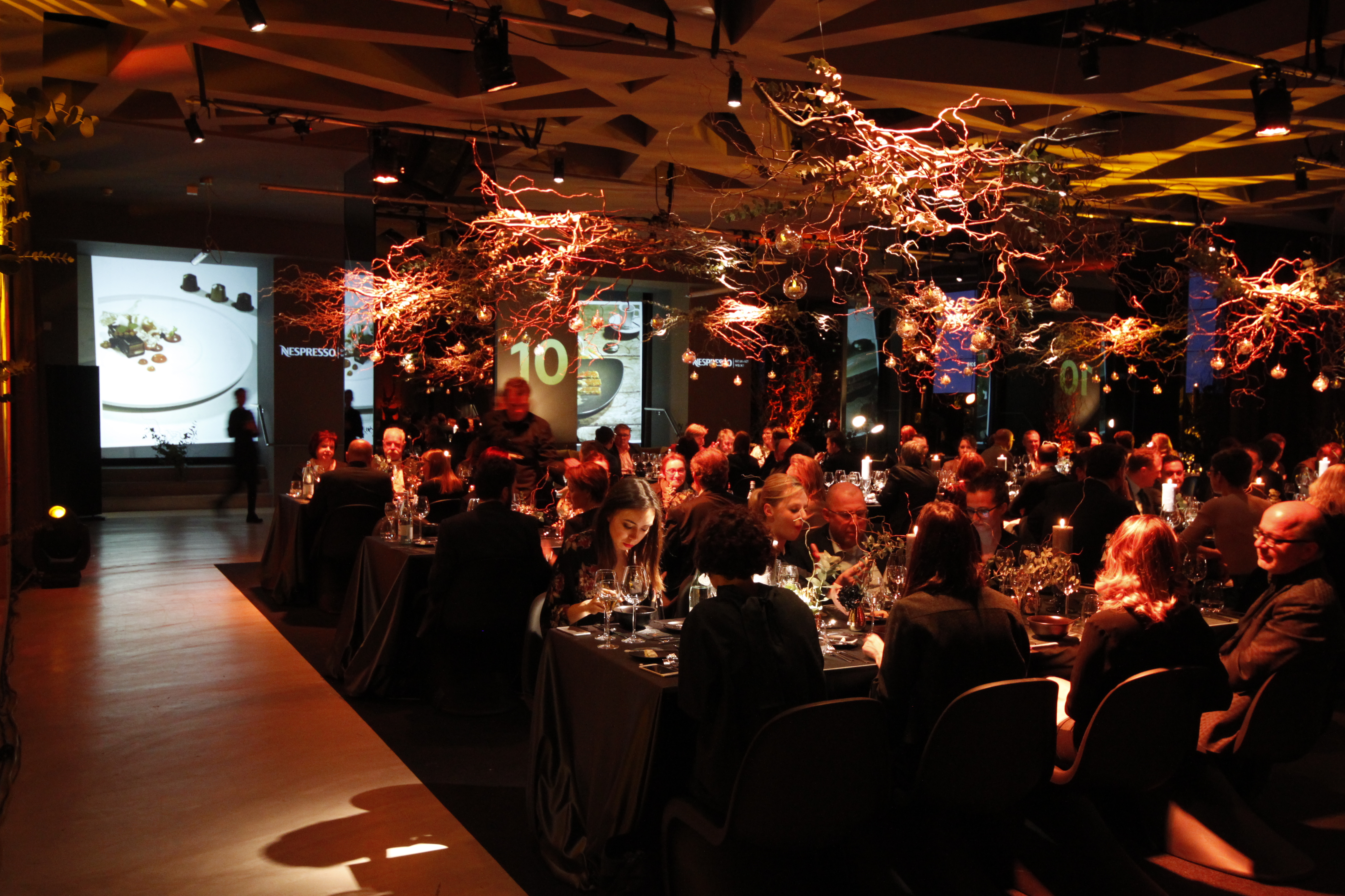 Dining tables beneath light installations in front of spatial projections – Nespresso, Palais Wertheim, Vienna, Austria