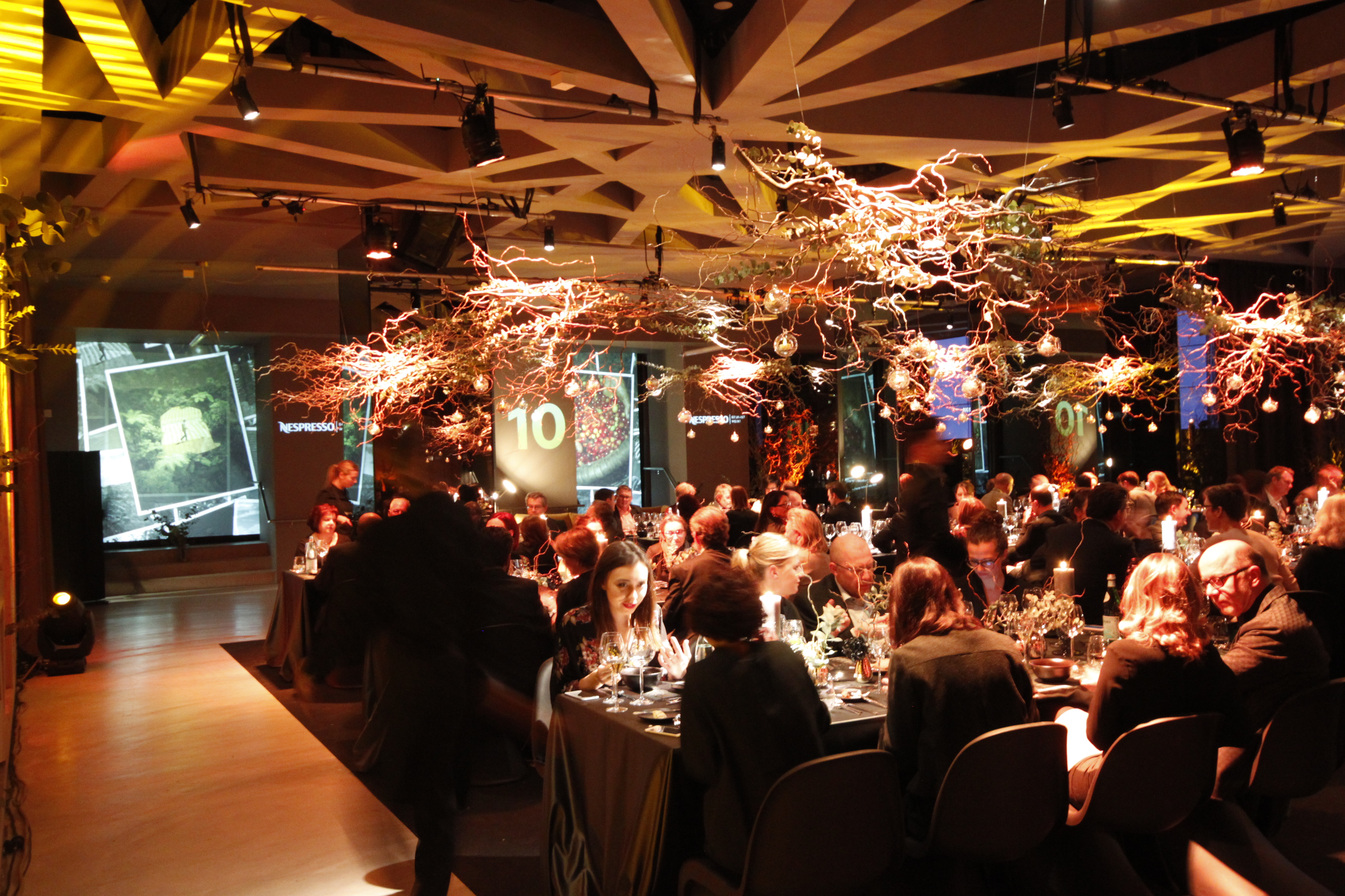 Dining tables beneath light installations in front of spatial projections – Nespresso, Palais Wertheim, Vienna, Austria